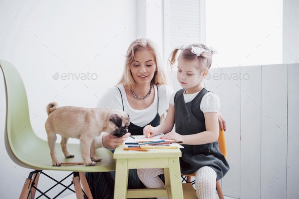 mother and child daughter draws are engaged in creativity in kindergarten. small pug with them