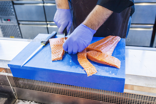 Midsection of fish vendor cutting salmon at refrigerated section in supermarket