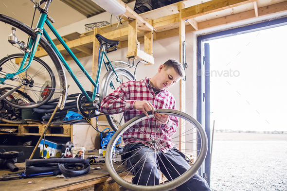 Man repairing bicycle tire while sitting by doorway in workshop