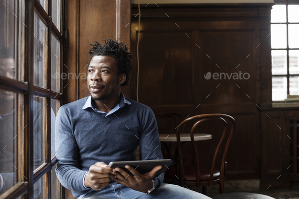 Young man looking through window while using tablet at cafe