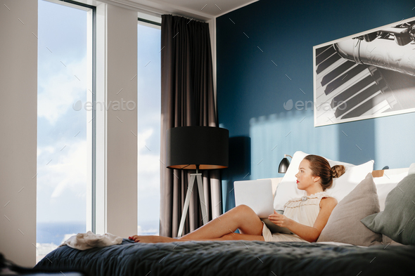 Businesswoman relaxing on bed while looking through window at hotel room