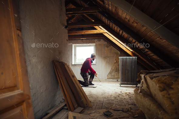 Man measuring floor with tape measure in attic under renovation