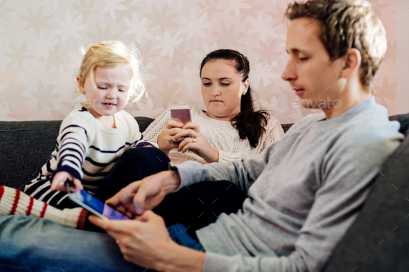 Girl sitting besides parents using technologies at home