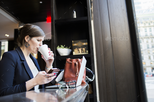 Businesswoman drinking coffee while using technologies at coffee shop