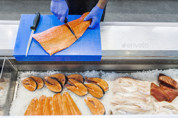 Cropped image of fish vendor cutting salmon at refrigerated section in supermarket
