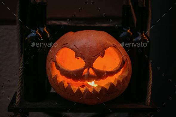 Pumpkin with scary carved glowing face and candle light in dark, modern festive decoration
