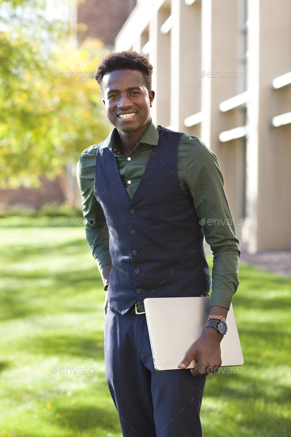 Handsome young black student holding laptop on a school campus