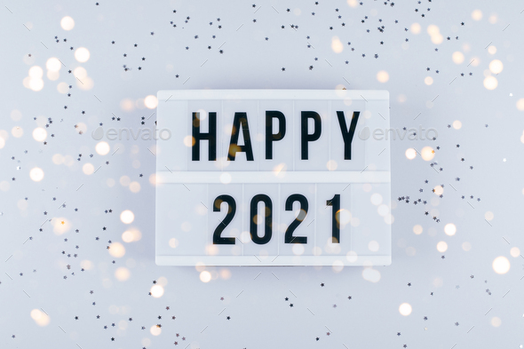 Happy New Year 2021 celebration. Light box with text Happy 2021 and sparkles on grey background.