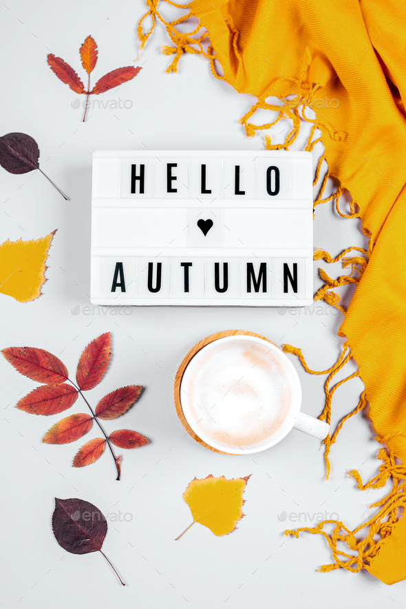 Cup of coffee, orange scafr and light box words Hello Autumn and autumn leaves on grey background