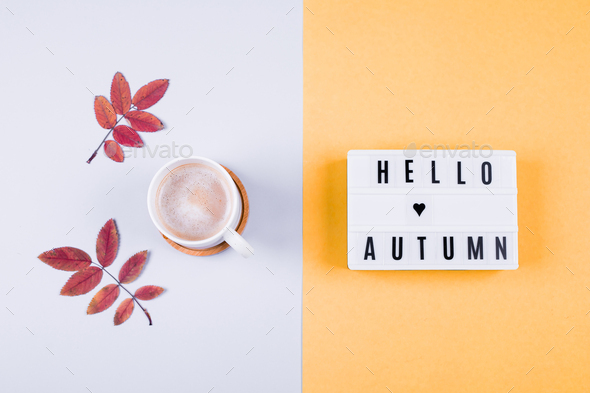 Light box the words Hello Autumn, cup of coffee on yellow grey background. Cozy mood season concept.