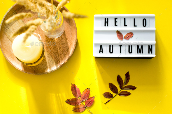 Light box words Hello Autumn on yellow background. Colorful autumn leaf, candle and dried flowers