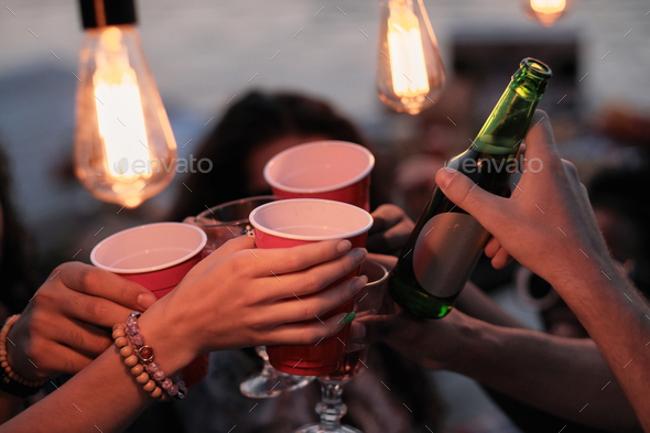 Close-up of young people holding glasses with beer and toasting with them during a party