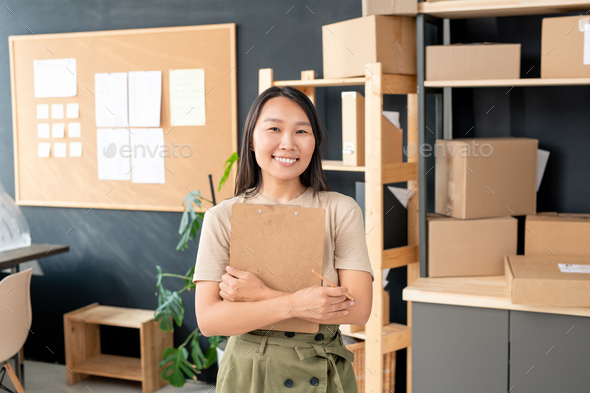 Young smiling Asian female with pencil and clipboard standing in front of camera