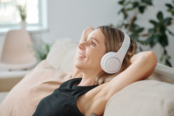 Side view of young blond smiling woman in headphones enjoying music