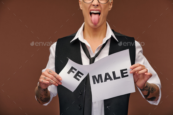 Aggressive woman in formalwear showing her tongue and tearing off syllable fe from word female on paper so that it became male