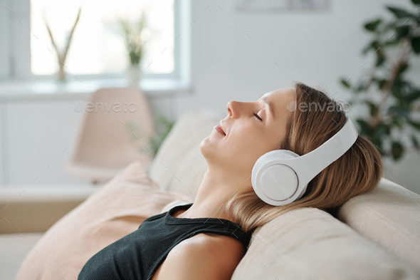 Side view of young relaxed woman in headphones lying on back of couch