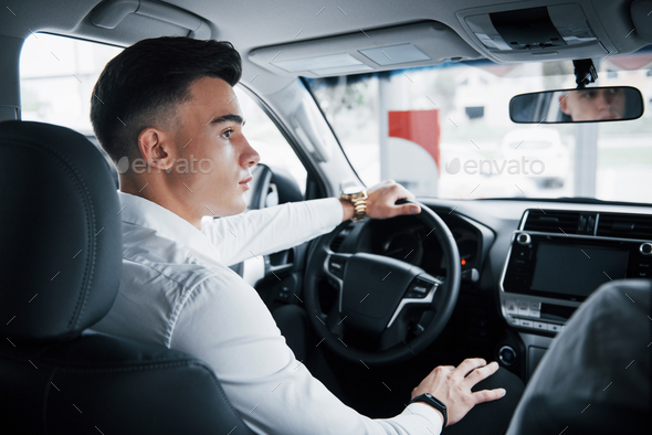 A young man sits in a newly purchased car at the wheel, a successful purchase