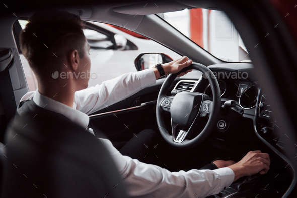 A young man sits in a newly purchased car at the wheel, a successful purchase