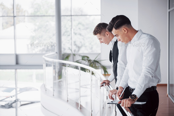 Young business people looking at documents and products standing at the office railing.