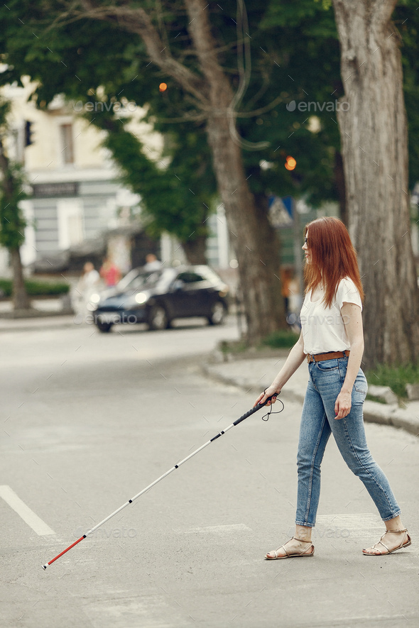 Young blind person with long cane walking in a city