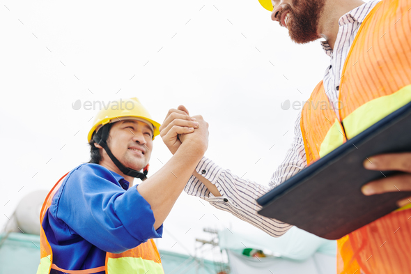 Happy contractor and head engineer shaking hands after finishing work on big object