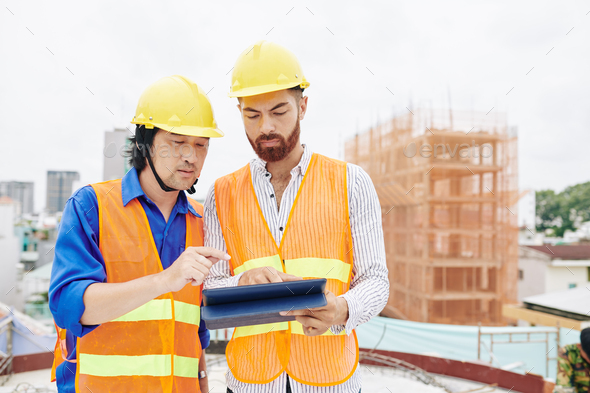 Serious multi-ethnic contractor and builder discussing blueprint or work schedule on tablet computer