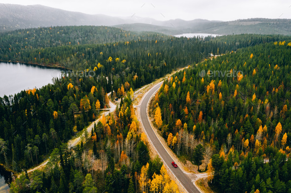 Aerial view of rural road with red car in yellow and orange autumn forest with blue lake - Stock Photo - Images