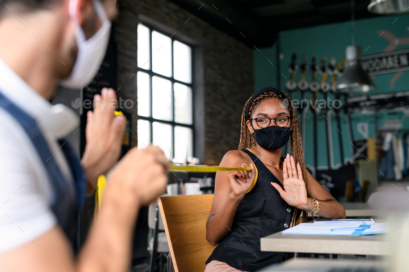 Young businesspeople with face masks working indoors in office, keeping safe distance