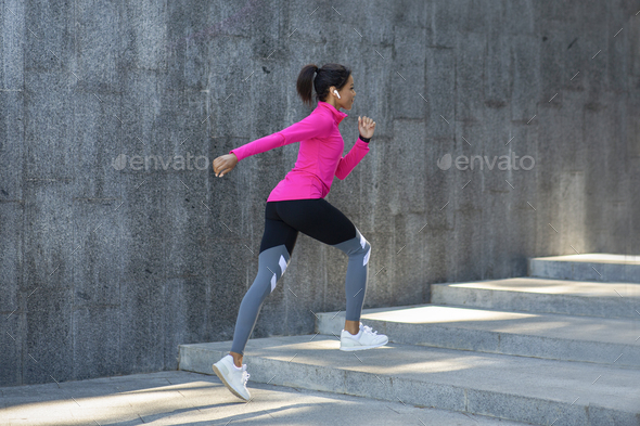 African woman in sportswear jogging at public park, empty space, side view