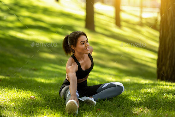 Healthy african woman warming up on the grass before jogging by park, free space