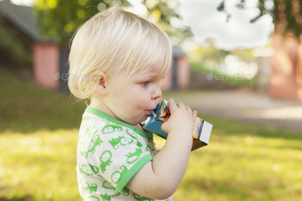 Side view of cute baby boy drinking from juice box at park