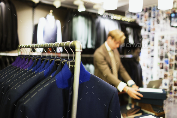 Close-up of suit rack at clothing store with designer working in background