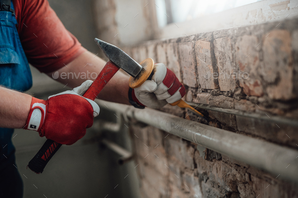 Worker’s gloved hands with hammer and chisel, getting rid of plaster on a brick wall