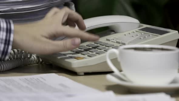 Office worker uses a landline phone to answer incoming calls and dialing a number to make a call alt
