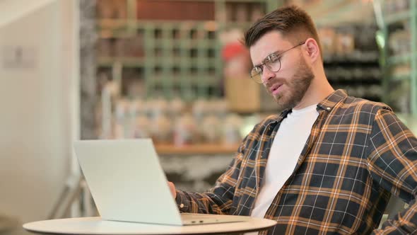 Young Man with Back Pain Using Laptop in Cafe alt