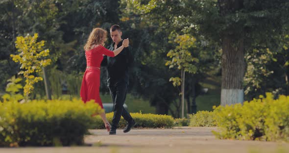 Beautiful Woman in a Red Suit and a Guy Dancing in a Pair Tango in the Park