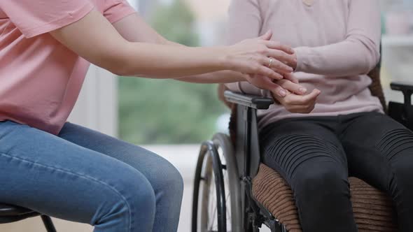 Unrecognizable Young Paralyzed Woman and Friend Holding Hands Sitting Indoors alt