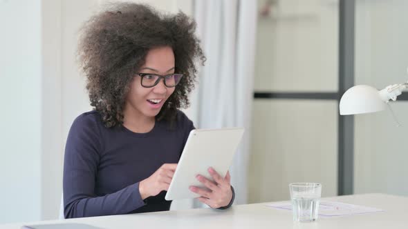 Successful African Woman Celebrating on Tablet at Work alt
