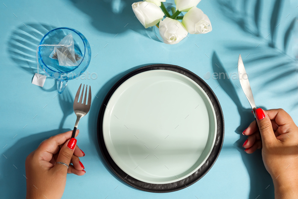 Dinner table with ceramic plate and woman hand holding knife and fork - Stock Photo - Images