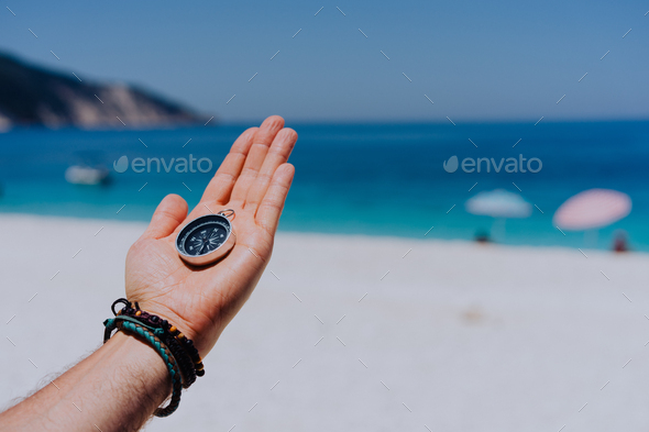 Stretched hand palm with black metal compass against sandy beach and blue sea. Follow your way, goal