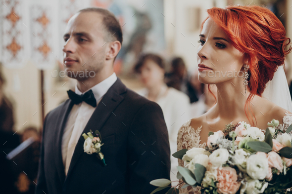 Stylish happy bride holding modern bouquet and looking at groom