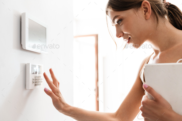 Young woman entering code on keypad of home security alarm - Stock Photo - Images