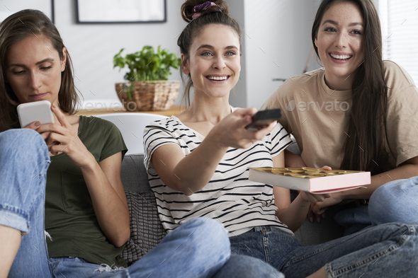 Three friends watching TV with a box of chocolates