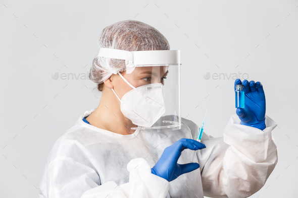 Medical workers, covid-19 pandemic, coronavirus concept. Profile of lab tech, female doctor or scientist in personal protective equipment, holding vaccine ampoule and syringe, grey background.