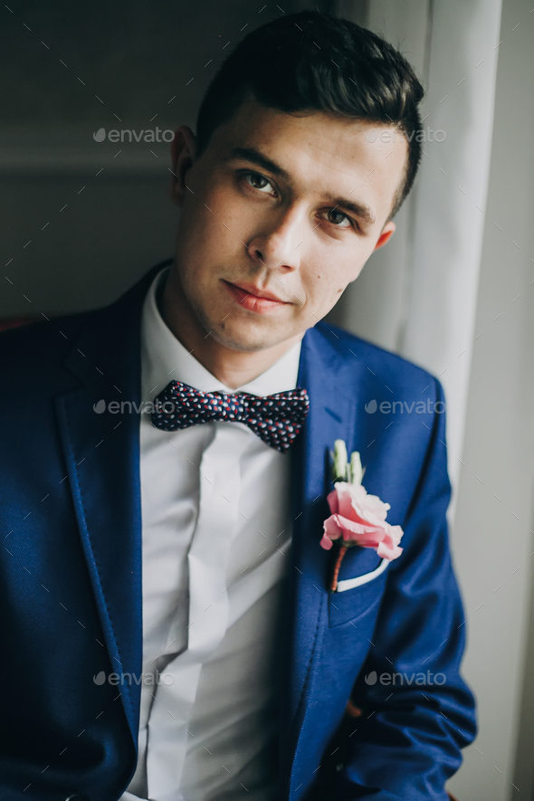 diagonal Refrigerar Tumor maligno Groom in blue suit, with bow tie and boutonniere with pink rose posing near  window Stock Photo by Sonyachny