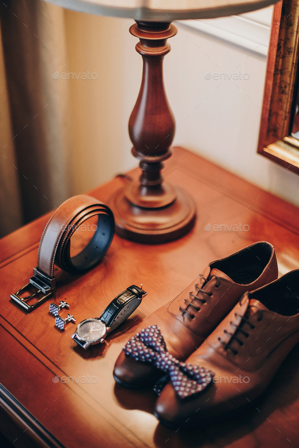 Stylish watch and expensive brown shoes for groom on wooden table in hotel room