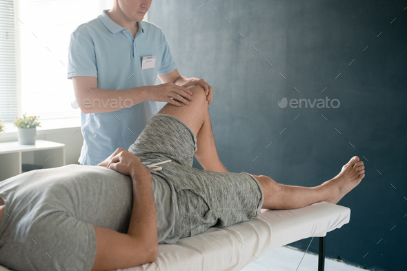 Male patient lying on couch while physiotherapist massaging his bent left knee