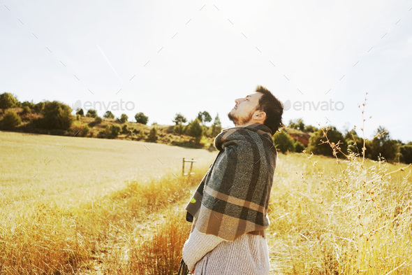 Side of a stand young man enjoying in calm the morning autumn sun in a path of a yellow field with the backlight from the blue sky