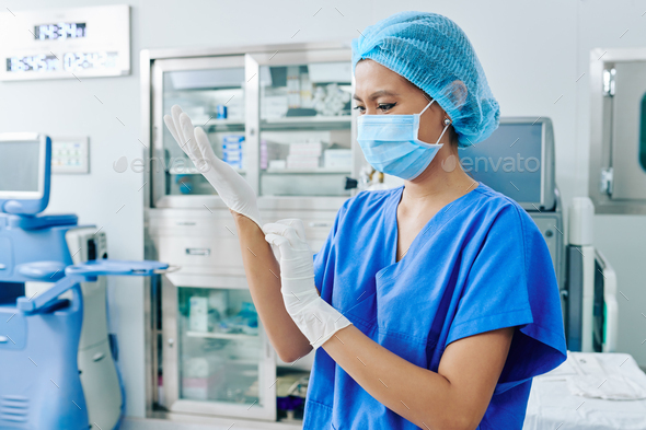 Vietnamese female surgeon in medical mask putting on rubber gloves and getting ready for surgery