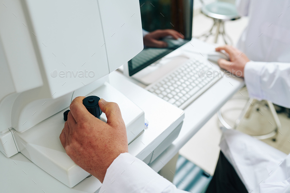 Eye specialist in ophthalmology clinic examining patient with non-mydriatic retinal camera and checking results on computer